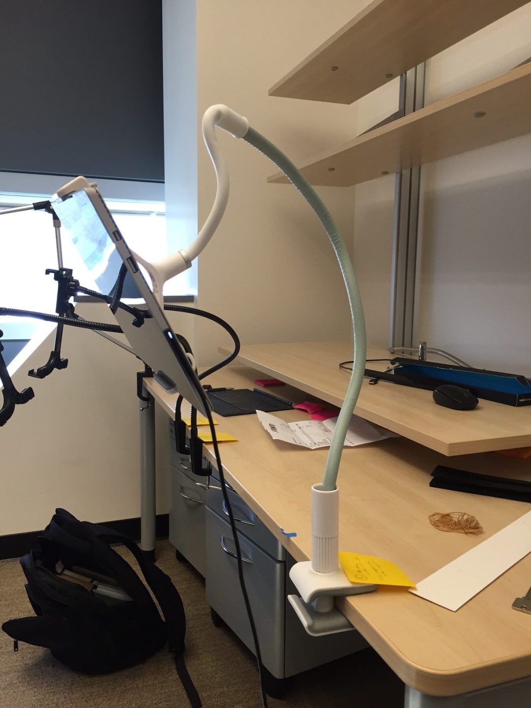 A lab desk with a tablet and eye tracker held on articulated gooseneck mounts clamped to the table edge.