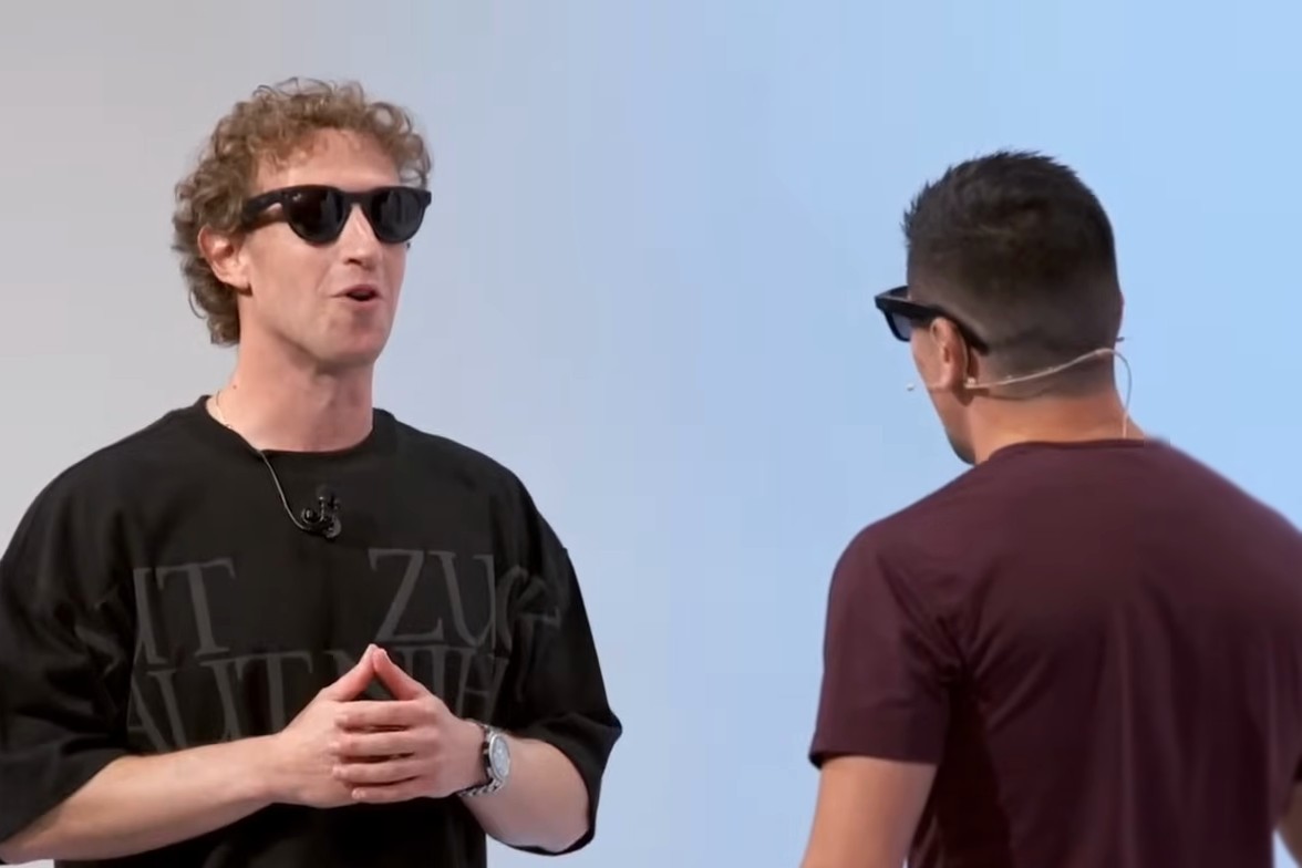 Mark Zuckerberg and mixed martial artist Brandon Moreno, both wearing Ray-Ban Meta glasses, laugh on stage while a screen behind them shows their conversation translated between English and Spanish.